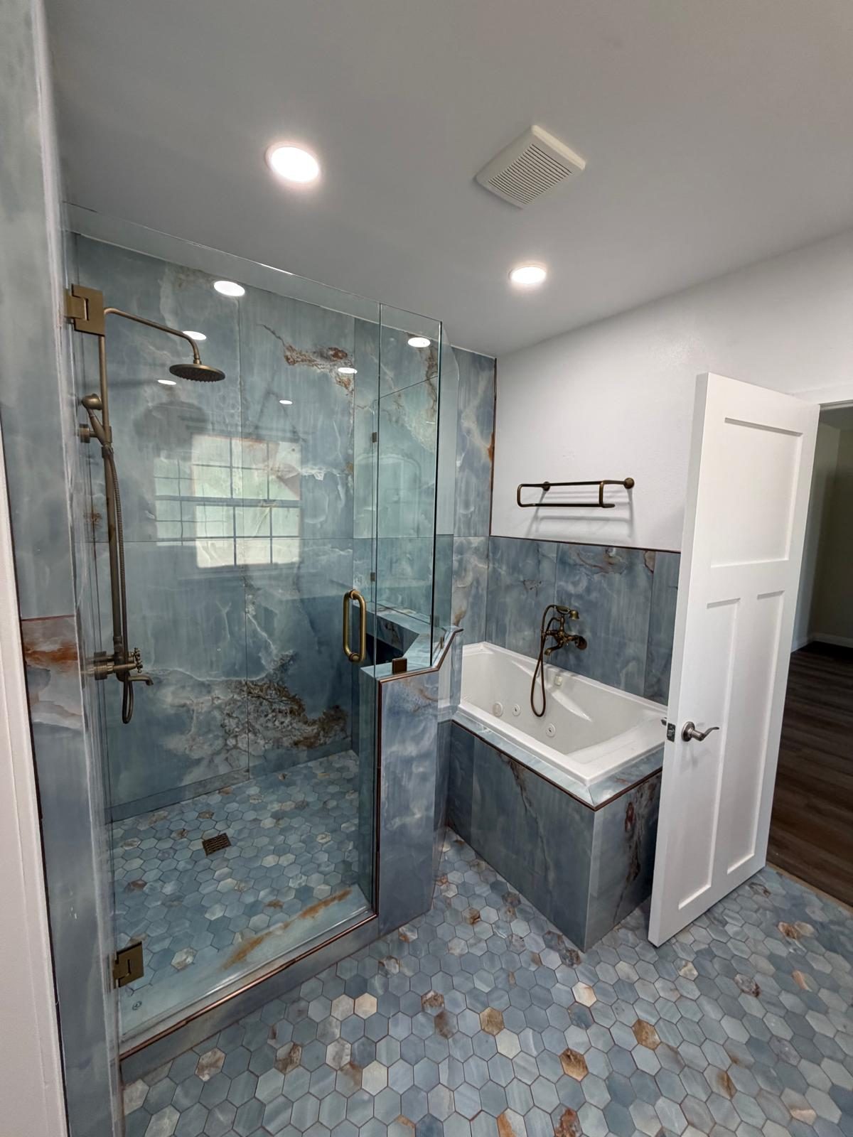 Glass shower with blue stone tile, brass fixtures, and a soaking tub